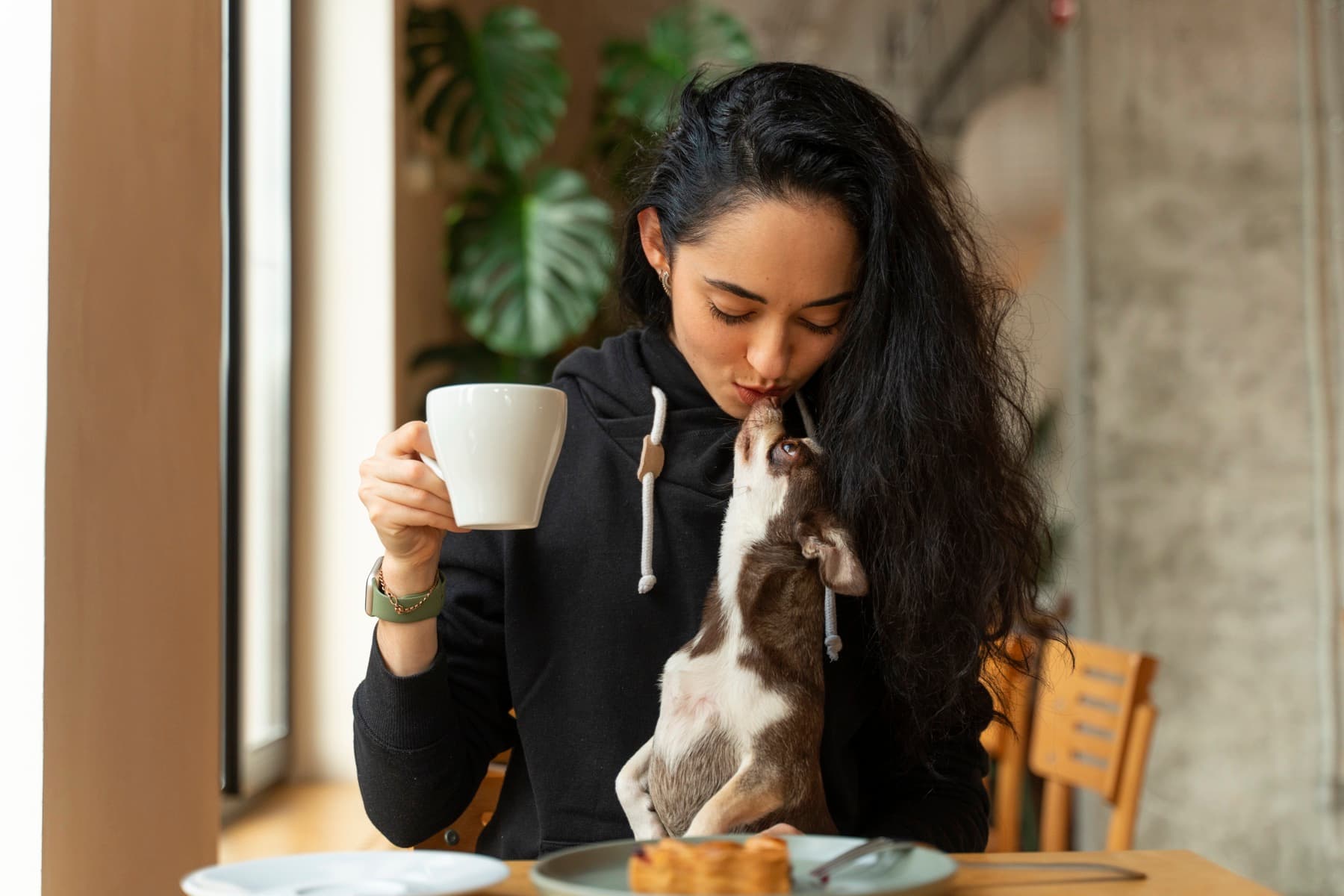 Una mujer besa a su chihuahua mientras toma un café