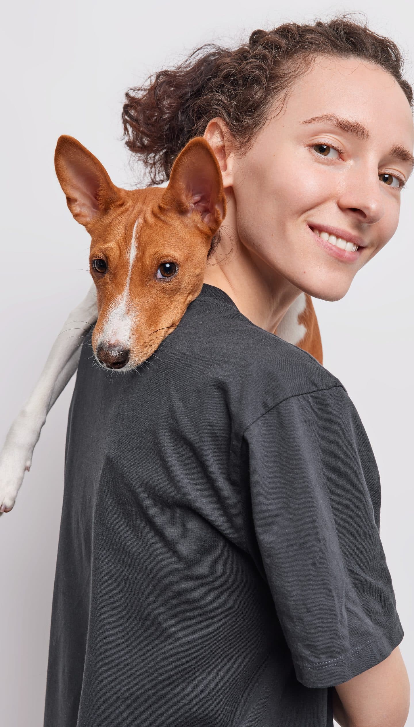 Una mujer sonríe con su perro basenji apoyado en el hombro